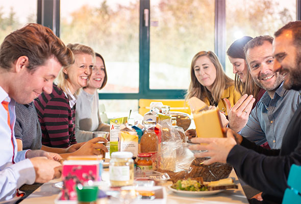 Group of people sat around table smiling and eating lunch